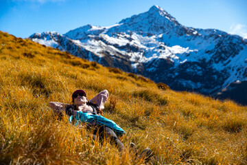 Relaxed hiker girl lies on alpine meadow resting, admiring surrounding mountain views near Avalanche Peak, Arthur's Pass National Park, Canterbury, South Island, New Zealand
