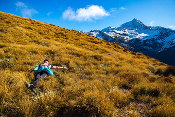 Relaxed hiker girl lies on alpine meadow resting, admiring surrounding mountain views near Avalanche Peak, Arthur's Pass National Park, Canterbury, South Island, New Zealand