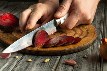 A person is carefully slicing vibrant beetroot into thin rounds on a rustic wooden board. The...
