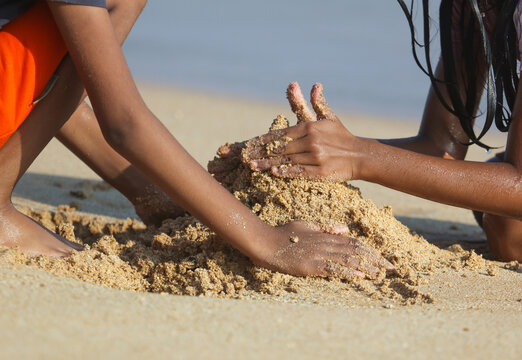 Two children are playing in the sand, one of them building a sandcastle