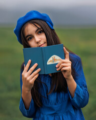 Vintage girl in blue dress and beret holding book in countryside field