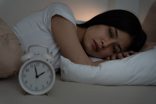 asian woman in bed late trying to sleep suffering insomnia, sleepless or scared in a nightmare, looking sad worried and stressed. Tired and headache or migraine waking up in the middle of the night.