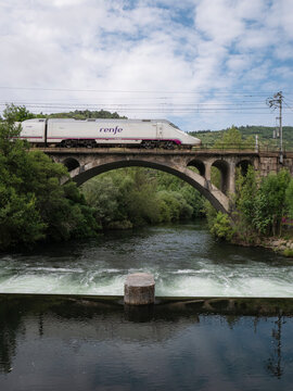 Ponferrada, Leon, Spain; 06-15-2025: The Renfe Alvia train of the Spanish public operator Renfe Viajeros enters Ponferrada station, passing over a bridge and leaving its reflection in the Sil River