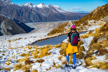 Brave hiker girl admires alpine mountain landscapes and glacial tarn lake on trail to Mueller Hut, Aoraki Mount Cook National Park, Canterbury, South Island, New Zealand
