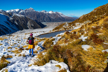 Brave hiker girl admires alpine mountain landscapes and glacial tarn lake on trail to Mueller Hut, Aoraki Mount Cook National Park, Canterbury, South Island, New Zealand