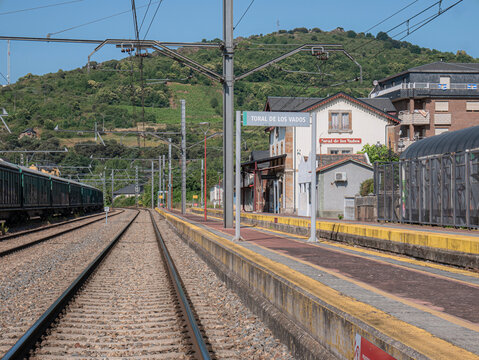 Toral de los Vados, Leon, Spain, 06-16-2025: Main track of the station between the passenger building and some parked cars and a high signal in the background with the red light on indicating a stop