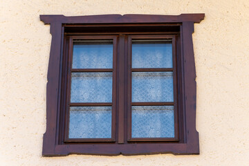 Antique wooden window with carved frame - classic window with openwork curtains against a warm textured wall.
