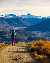 Hiker girl hikes along Roys Peak trail and admires stunning panoramic views over Lake Wanaka and surrounding alpine peaks near Wanaka, Otago, South Island, New Zealand.