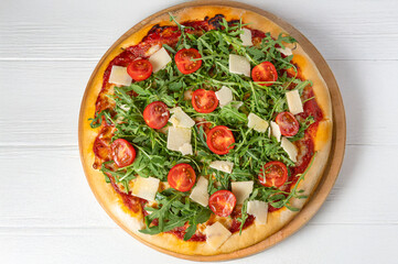 Italian pizza with tomato sauce, mozzarella, fresh cherry tomatoes, arugula, and Parmesan shavings, shot from above on a white wooden background. Horizontal, natural light, vibrant colors