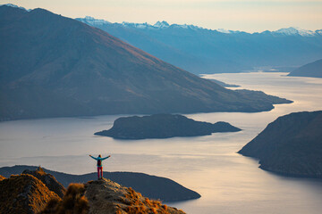 Hiker woman admires breathtaking panoramic view over Lake Wanaka and surrounding snow covered peaks from viewpoint on way to Roys Peak summit near Wanaka, Otago, South Island, New Zealand.