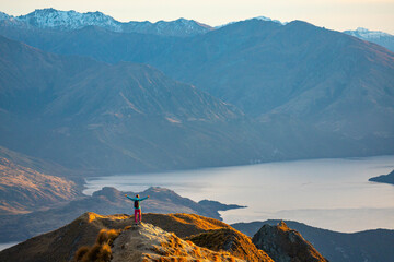 Hiker woman admires breathtaking panoramic view over Lake Wanaka and surrounding snow covered peaks from viewpoint on way to Roys Peak summit near Wanaka, Otago, South Island, New Zealand.