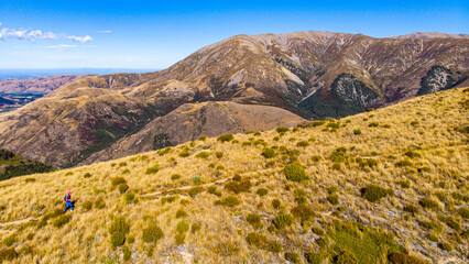 Aerial view of hiker woman ascending towards Trig M summit via Porters Pass with Lake Lyndon and Torlesse Tussocklands, Canterbury, South Island, New Zealand.