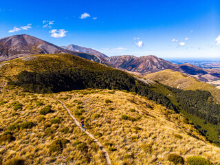 Aerial view of hiker woman ascending towards Trig M summit via Porters Pass with Lake Lyndon and Torlesse Tussocklands, Canterbury, South Island, New Zealand.