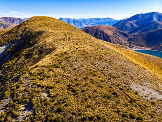 Aerial view of hiker woman ascending towards Trig M summit via Porters Pass with Lake Lyndon and Torlesse Tussocklands, Canterbury, South Island, New Zealand.