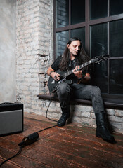 Young rock musician (headbanger) playing an electric guitar. Portrait of a handsome long-haired...