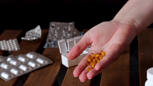 closeup of hand holding translucent yellow capsules near pill container and scattered medication packaging