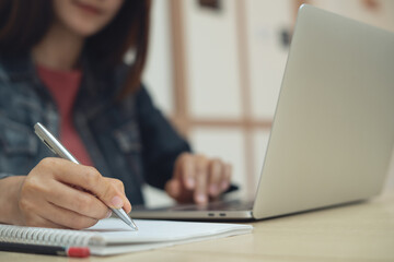 Business woman working on laptop computer and writing on notebook. Female student searching the...