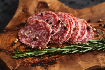 Sliced salame milano sausage on olive wood board with rosemary and pepper
