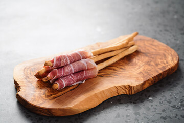 Grissini with prosciutto on olive wood board