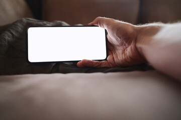 man hand holding phone with white screen over bed on background
