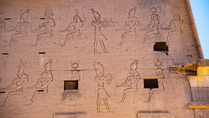 wall reliefs on the first pylon of Edfu Temple in Egypt, depicting ancient Egyptian deities and the pharaoh