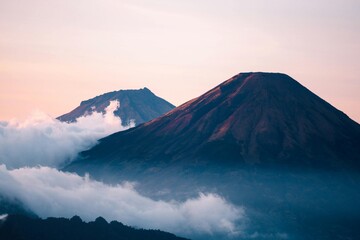Fototapeta premium Volcanoes Surrounded by Clouds Under a Pastel Sky at Sunrise