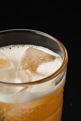 Close-up of a refreshing citrus drink with ice cubes and a frothy foam top in a textured glass,...