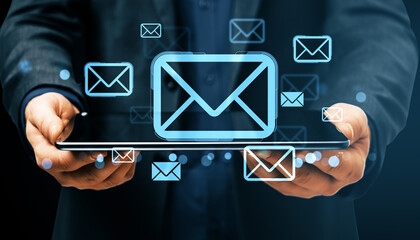 Digital email communication concept with glowing envelope icons displayed above a tablet held by a person in business attire on dark background.