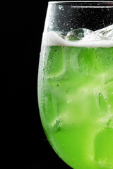 Close-up of a chilled green cocktail or soda with ice cubes and condensation in a glass, set against a black background. Perfect for summer, bar, or beverage concepts.