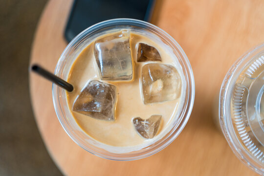 Refreshing iced coffee with milk in plastic cup on wood table. Top view