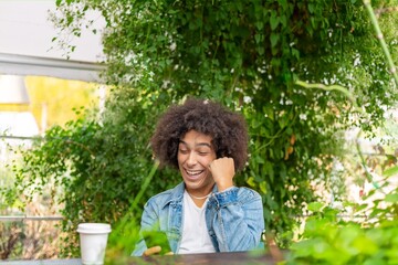 Smiling young mixed race Afro-Italian man rejoices in his successes and victories, showing a positive hand gesture, a lucky man who happily achieves goals and objectives in an eco-friendly green area