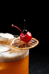 A refreshing orange cocktail topped with creamy foam, ice, a dried orange slice, and a maraschino...
