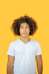  Beautiful young mixed race man in his 20s, . Portrait beautiful men of multiracial on a yellow background. A young ethnic man with curly hair in a white t-shirt looks relaxed