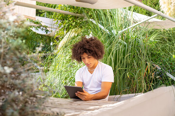 A young ethnic man digital tablet outdoors in a green area in nature. Free green open space place to work, business, study, freelancer coworking, in nature. Environmentally friendly working 