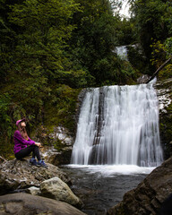 adventurous girl sits on rock and admires impressive powerful Ryde Falls up close. Best hidden gems/waterfalls near Oxford, Christchurch, canterbury, New Zealand, south island.