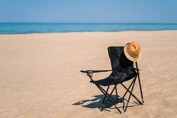 Beach chair on deserted sandy beach, straw hat on the back of the chair, hot afternoon and siesta time, copy space poster about vacation and relaxation in secluded places on the Mediterranean coast