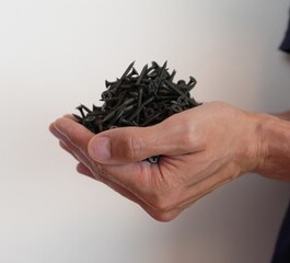 A close-up of men's hands holding several black screws against a white wall on the side. Metal...