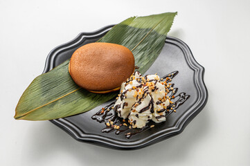 Japanese dorayaki with creamy vanilla gelato, chocolate drizzle, and hazelnut sprinkles on a sleek black plate, isolated on white. Horizontal, natural light, vibrant dessert display.

