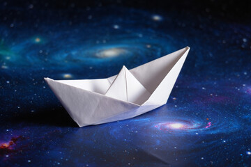 Obraz premium Serene White Origami Boat Sailing on a Cosmic Galaxy Background: Hope, Dreams, and Exploration Concept