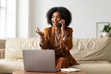 African american woman on phone call working from home with laptop and notebook on desk