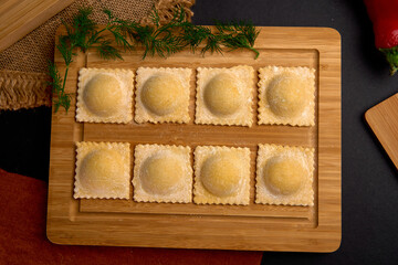 Delicious Freshly Made Ravioli on a Wooden Board with Green Herbs and Red Peppers Nearby Capturing the Essence of Traditional Italian Cuisine