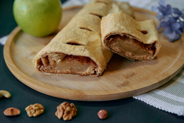 Deliciously Baked Apple Strudel on a Wooden Plate with Fresh Green Apple and Assorted Nuts Perfectly Arranged for a Tasty Treat Experience