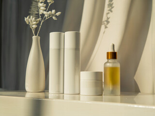 Minimalist skincare bottles and serum dropper in golden light with ceramic vase and soft draped background for clean beauty branding