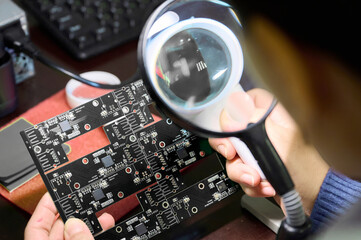 Close examination of electronic circuit board with magnifying glass in workshop