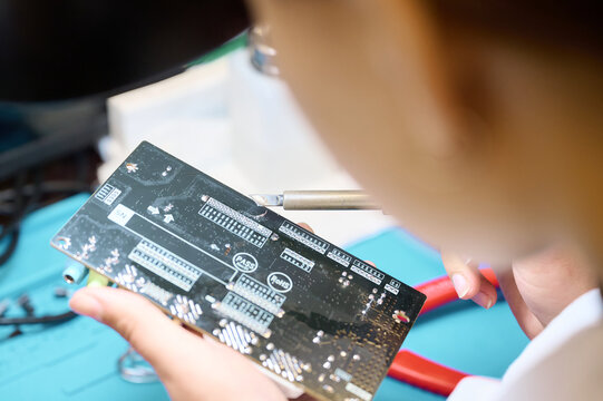 Technician soldering components on a circuit board in a workshop during a bright afternoon