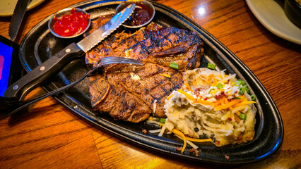 juicy grilled T bone steak, perfectly seared, served alongside a loaded baked mash potato on a warmly lit rustic dining setup. Ideal for culinary content