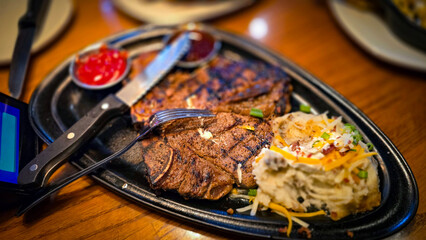 juicy grilled T bone steak, perfectly seared, served alongside a loaded baked mash potato on a warmly lit rustic dining setup. Ideal for culinary content