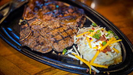 juicy grilled T bone steak, perfectly seared, served alongside a loaded baked mash potato on a warmly lit rustic dining setup. Ideal for culinary content