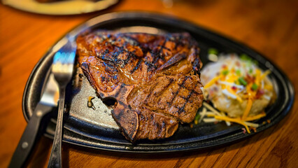 juicy grilled T bone steak, perfectly seared, served alongside a loaded baked mash potato on a warmly lit rustic dining setup. Ideal for culinary content