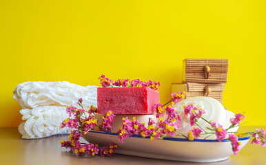 Diferentes jabones artesanales con flores sobre plato de cerámica sobre fondo amarillo.